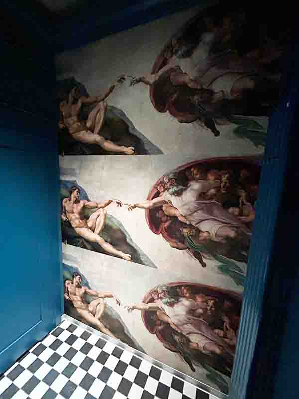 RAGU Michal aniol Ściana w toalecie RAGU Leszno z potrójnym motywem graficznym Stworzenia Adama Michała Anioła na niebieskim tle.