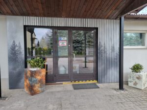 Nowoczesne wejście do budynku z panelami dekoracyjnymi, lamelami elewacyjnymi i donicą SmartFresk